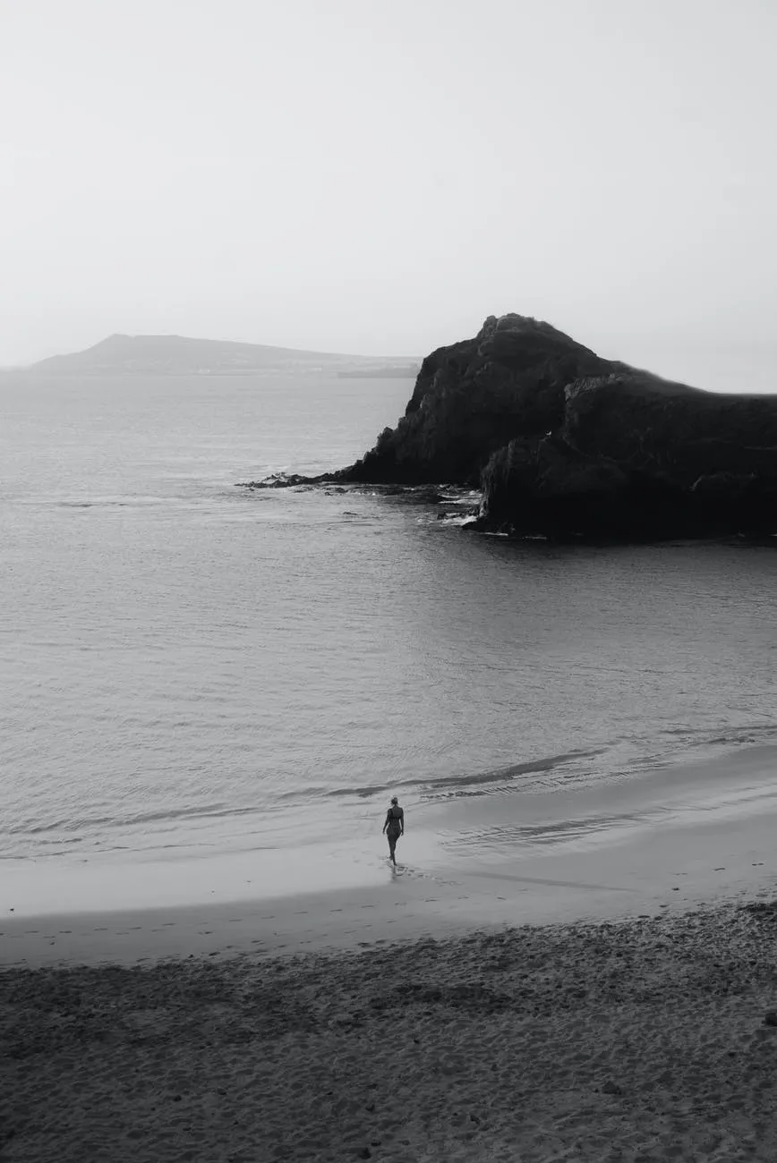 Beach with mountains in the distance and a lone figure walking into the water